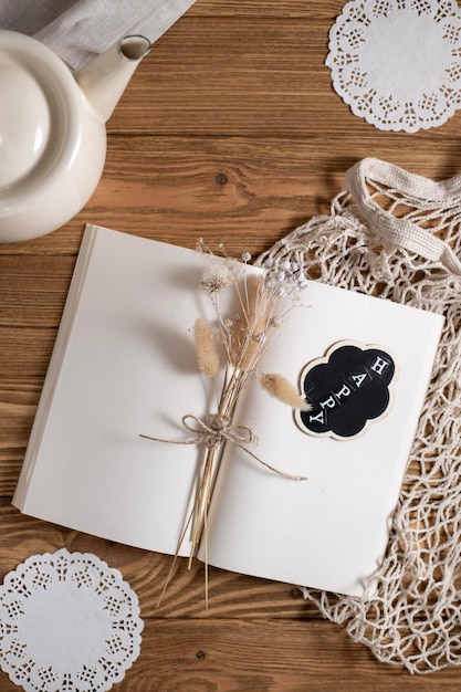 On the table is an open notebook with blank pages and a bouquet of dried flowers