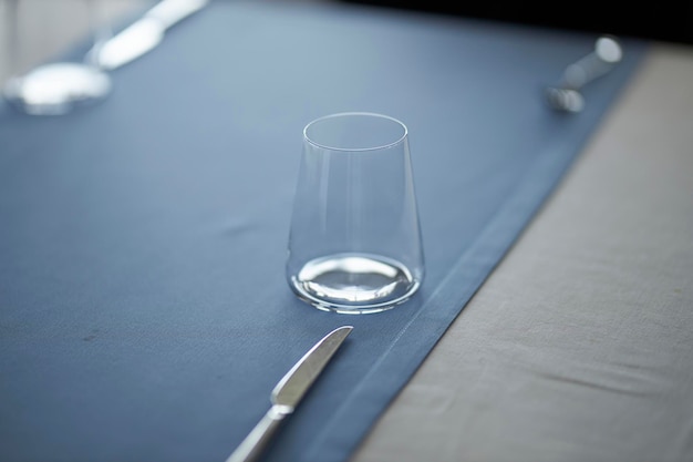 The table is set in a stylish and minimalistic way glasses on a\
blue tablecloth