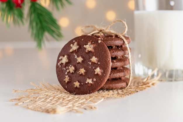 On the table is a stack of round chocolate christmas cookies and glass of milk