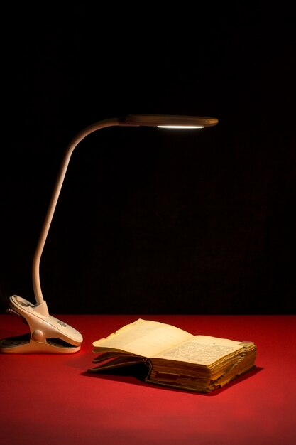 Настольная лампа освещает раскрытую книгу на красном столе
