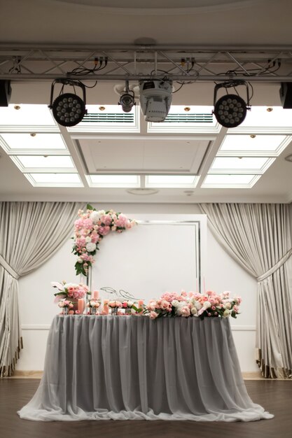 The table for the newlyweds is decorated with fresh flowers in the restaurant. Square lighting and spotlights