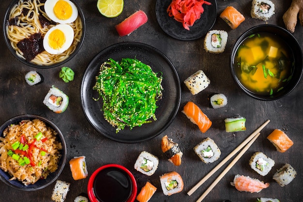 Table served with sushi and traditional japanese food on dark background.