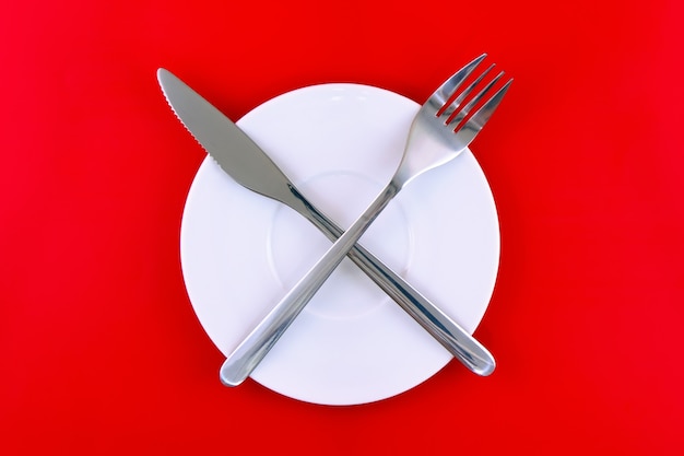 Table serving-knife,plate,fork on  red colour background.