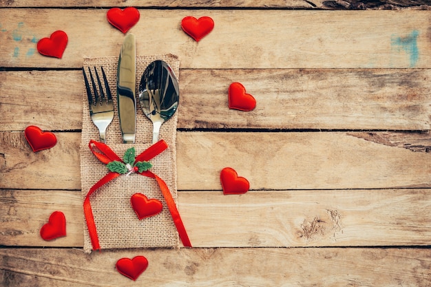 Table set for celebration Valentine's Day. Wooden table place setting and silverware with red heart for Valentine day.