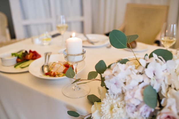 Table set at the wedding Banquet in the restaurant, classic style with white tablecloths and napkins, vases with flowers.