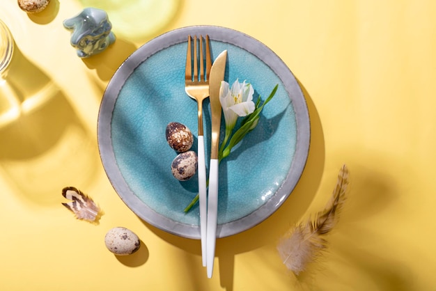 Table setting for celebrating easter plate cutlery eggs and spring flowers on the yellow table top