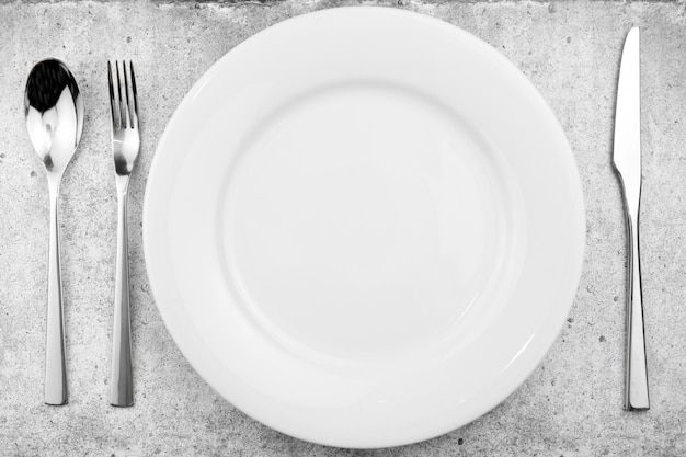 Table setting. Empty plate, knife, fork and a spoon on a light concrete 