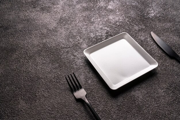 Table setting. A small white square plate and a fork and knife. grey background copy space.