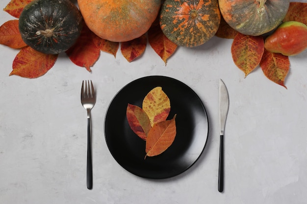 Table setting on Thanksgiving Day decorated pumpkin, pears and colorful leaves on grey. View from above