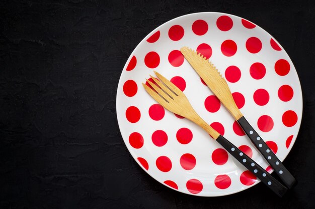 Foto regolazione della tavola con un coltello, una forchetta e un piatto di bambù con i pois su un fondo scuro
