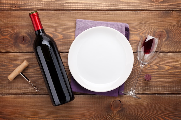 Table setting with empty plate, wine glass and red wine bottle. View from above over rustic wooden table background