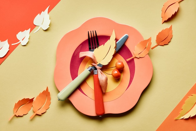 Table setup for Autumn celebration. Bright plastic plate on yellow paper with paper Autumn leaves