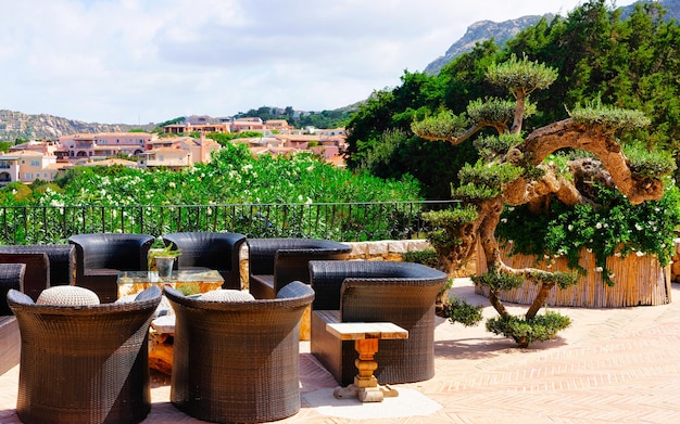 Table and sofa at porch of cafe or restaurant at costa smeralda\
luxury resort on sardinia island in italy in summer. cozy veranda\
with chair and umbrella at sardinian town in sardegna. mixed\
media.