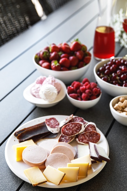 Table on the summer terrace is full of snacks. Cheese, sausage, salami, meat and berries.