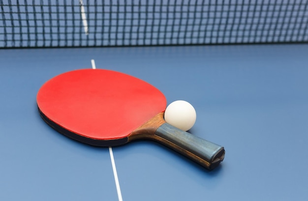 Table tennis racket white ball and net on a on blue board