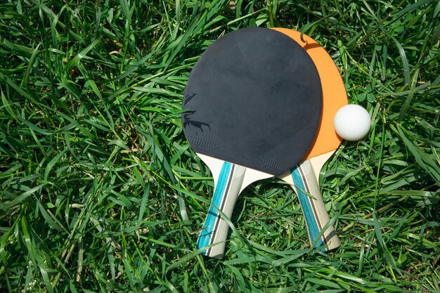 Table tennis rackets and a white plastic ball on the green grass background