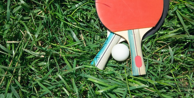 Table tennis rackets and a white plastic ball on the green grass background