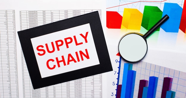 Sul tavolo sono riportati dei grafici multicolori, una lente di ingrandimento e un foglio di carta in una cornice nera con la scritta supply chain. concetto di affari