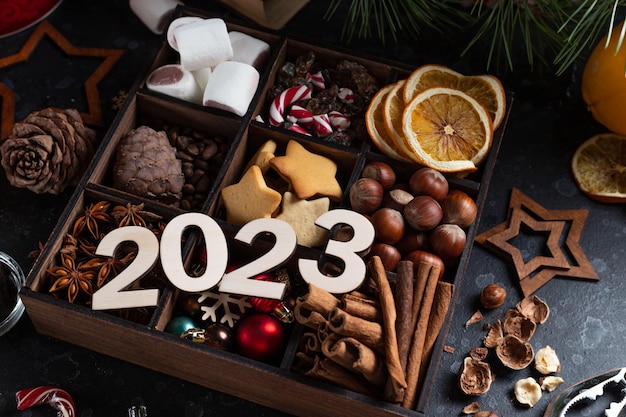 On the table there is a box with nine compartments in which nuts cookies and spices are poured On top are the numbers 2023