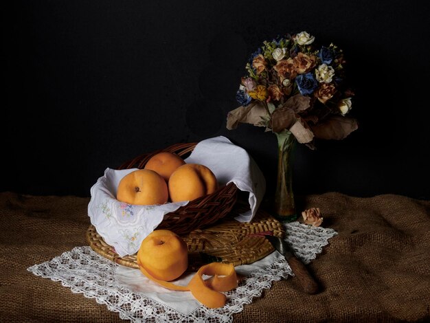 On a table there is a still life with a basket of peaches and a bouquet of flowers