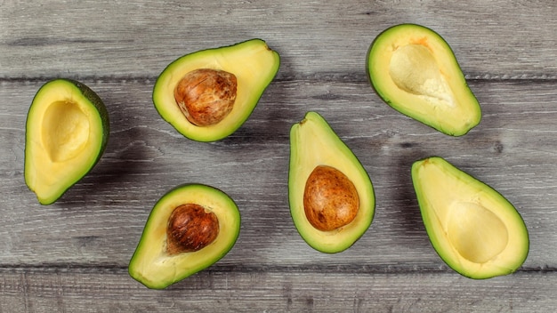 Table top view on arranged avocado halves, some of them with the seed, on wood desk.