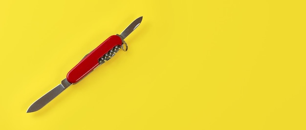 Вид сверху на стол, красный карманный нож с открытыми лезвиями, на желтой доске. Место для текста справа.