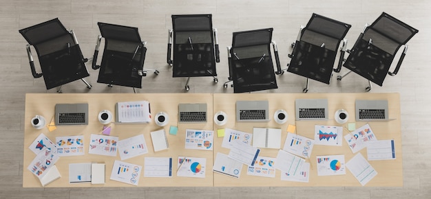 Table top view of wooden conference table with charts and graphs papers and laptop on it and six chairs lying in straight line beside the table in office. Concept for business meeting.