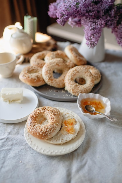 A table with bagels and a plate of butter and a spoon with a purple flower on it.