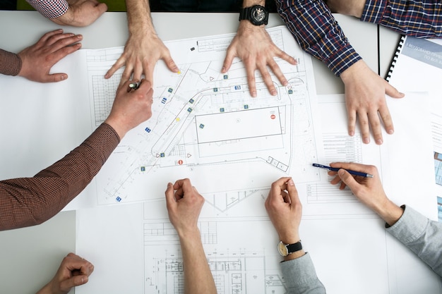 "Table with blueprints and hands holding pencils"