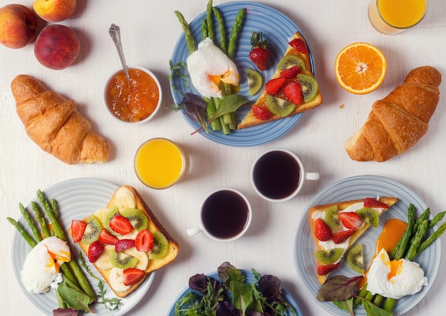 Table with breakfast - asparagus with poached eggs , toast with fruit, croissants, coffee, juice