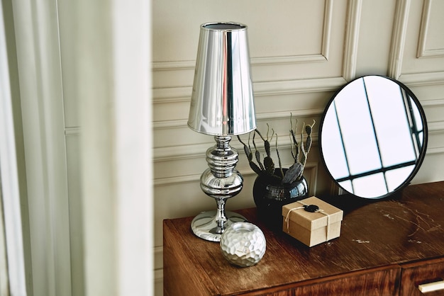 Table with lamp mirror and accessories on the background of wall decorated with moldings stylish modern interior design