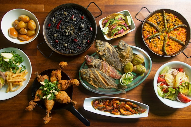 Table with meals from the sea and land, fried fish and paella.