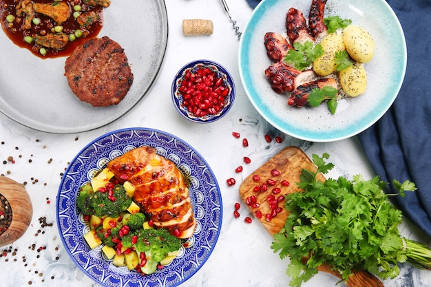 Table with meat meal and salad. octopus with potatoes and chicken with mango, meat pattie with peas and ingredients on table top view.