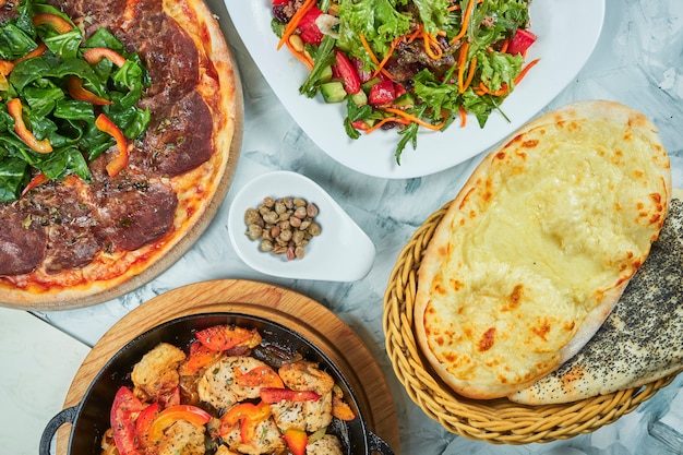 Table with planty of food for lunch, healthy salad, pizza with vitello tonatto veal and Meat chicken pan with tomatoes. Flat lay food table