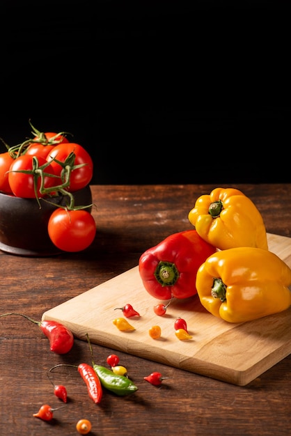 Tavolo con peperoni rossi e gialli peperoni cipolle e aglio e pomodori su legno rustico sfondo nero fuoco selettivo
