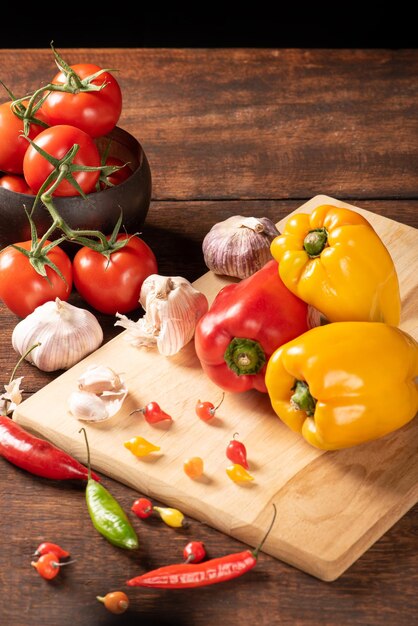 Table with red and yellow peppers peppers onions and garlic and tomatoes over rustic wood black background selective focus