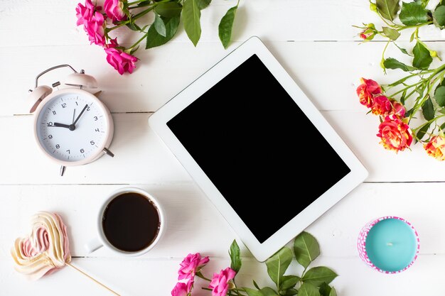 Tablet, alarm clock, cup of coffee, roses, candles on the table