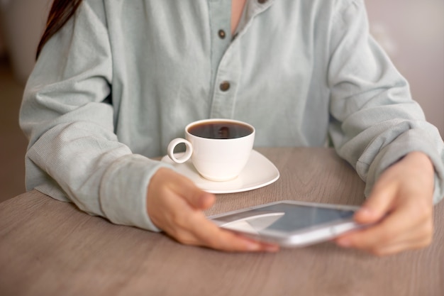 Tablet close up photo with woman in casual clothes at home or in cafe and drinking coffee