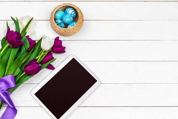 Tablet, colorful tulips and easter eggs on wooden surface