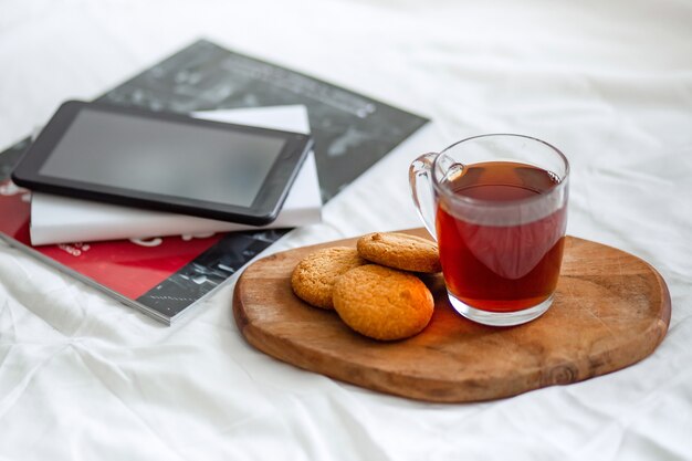 A tablet computer, a magazine, and a book on the bed.