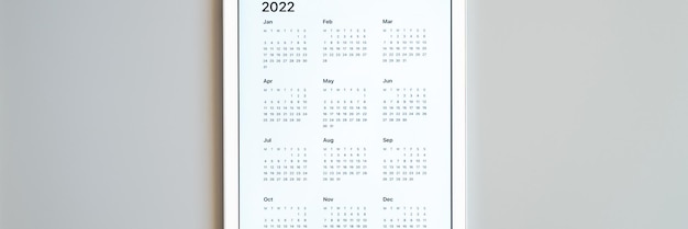 写真 灰色の背景に2022年のカレンダーの開いているアプリを備えたタブレットコンピューター。コンセプトビジネスまたはテクノロジーを使用してリストの目標を実行します。上面図、フラットレイ。バナー
