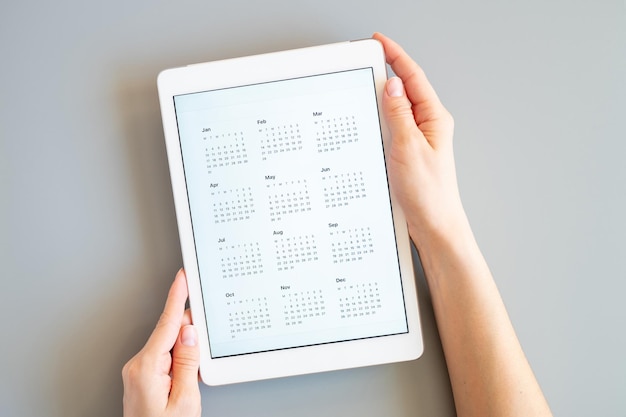 Tablet computer with an open app of calendar for unspecified unknown date year without date in a womans hands on a gray background concept business or to do list goals top view flat lay