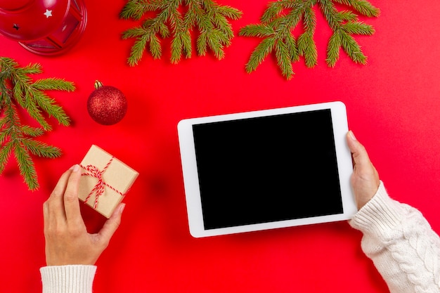 Tablet computer in woman hands over red with Christmas decoration