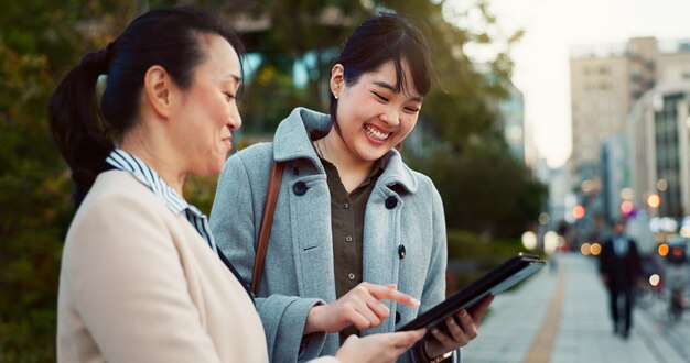 Tablet conversation and business women in the city talking for communication or bonding Smile discussion and professional Asian female people speaking with digital technology together in town