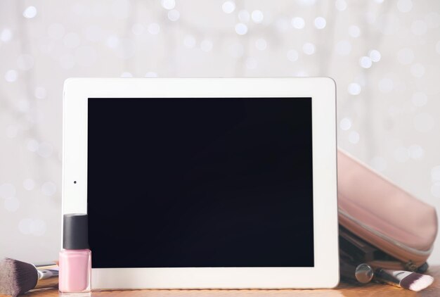 Tablet and cosmetics on color background