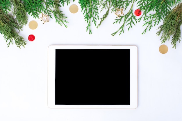 tablet display on table with isolated white screen for mockup in Christmas time. Christmas tree, gifts, decorations in background.