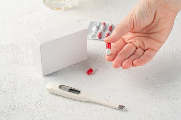 Photo tablet in a female hand on the table is a mockup of an empty white box for product packaging with medicines or vitamins place for logo and text