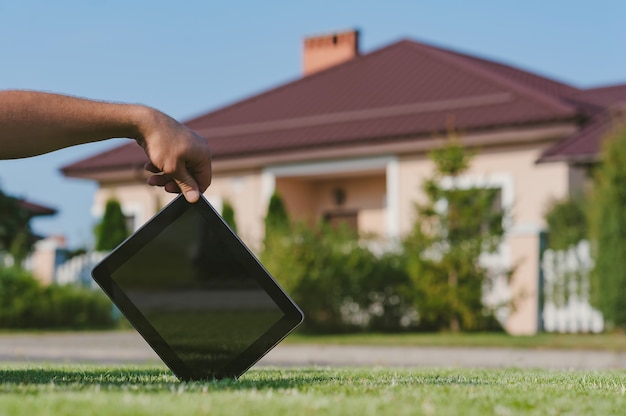 Tablet in de hand, op het grasveld tegen de achtergrond van het huis.