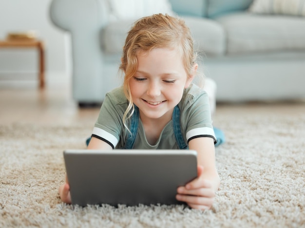 Tablet kind en online spel thuis met digitaal onderwijs leren en glimlachen van tech op tapijt woonkamer internet en e-learning app met jeugdontwikkeling of streaming kids film op website