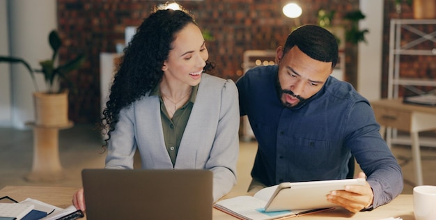 Tablet laptop and business people in office with ideas advice and late night collaboration at digital agency Teamwork man and woman with online research discussion and opinion at tech startup